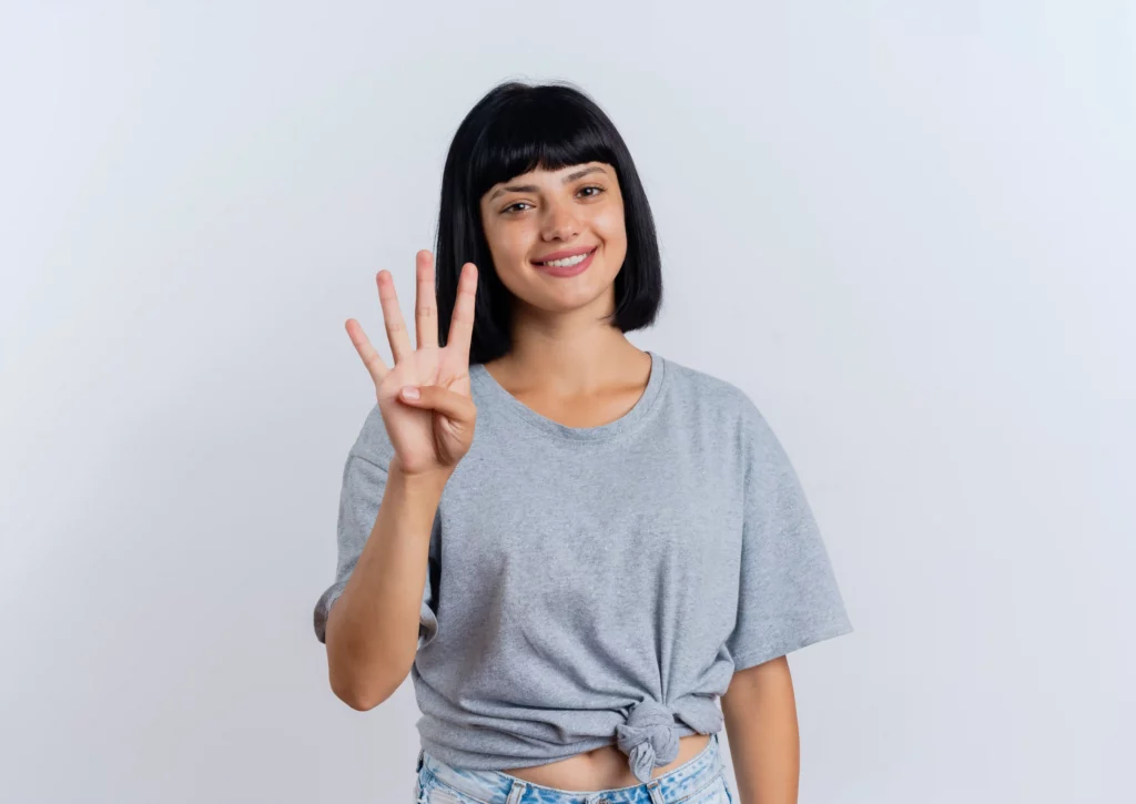 Woman in gray shirt holding up four fingers, smiling.