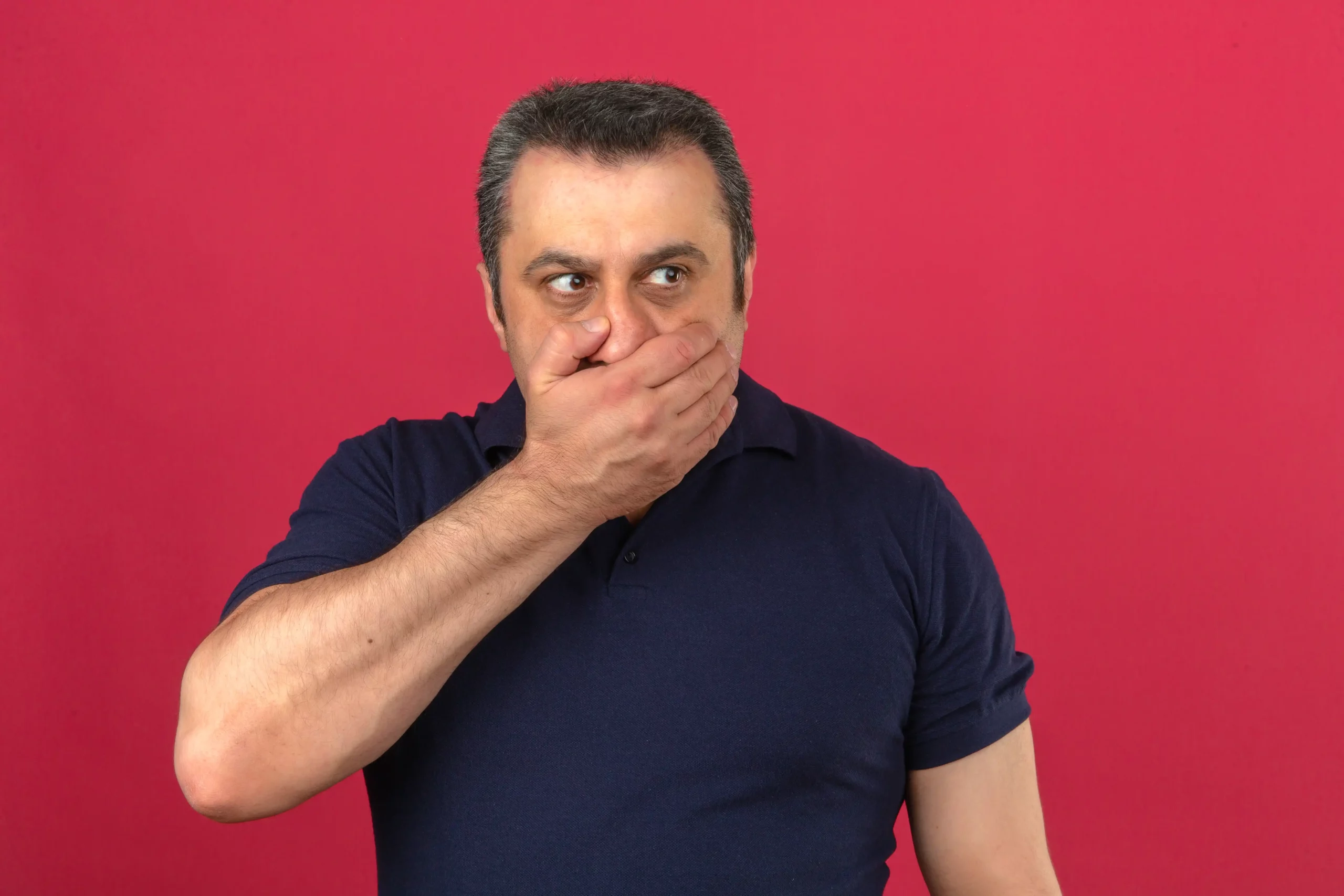 Man covering mouth reacting to strong burnt taste against solid red background