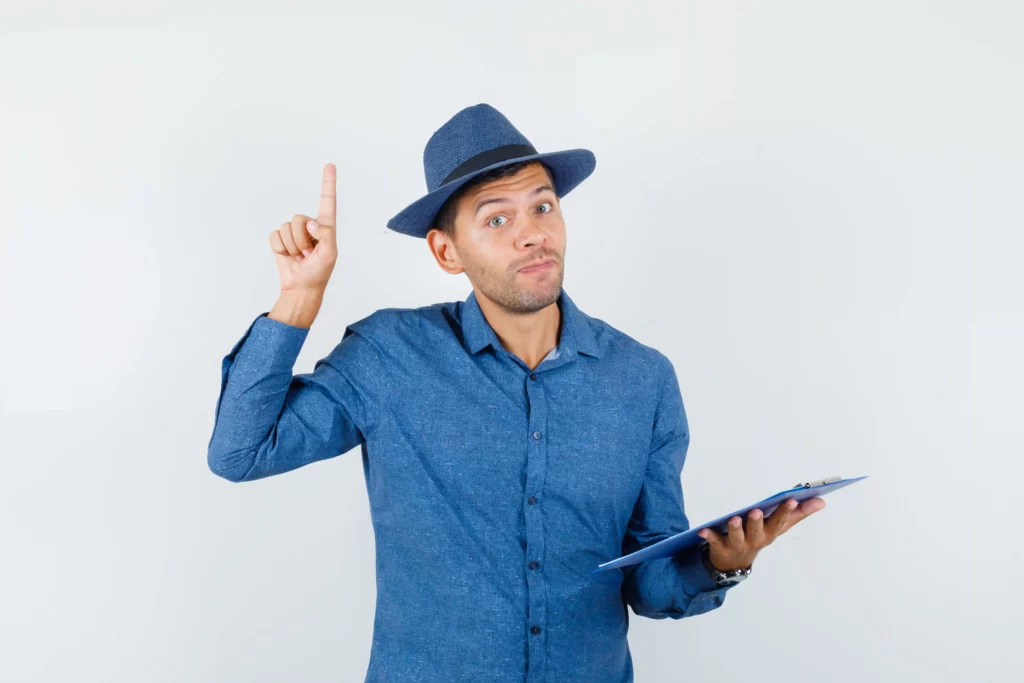 Person in blue shirt and hat holding clipboard, raising one finger.
