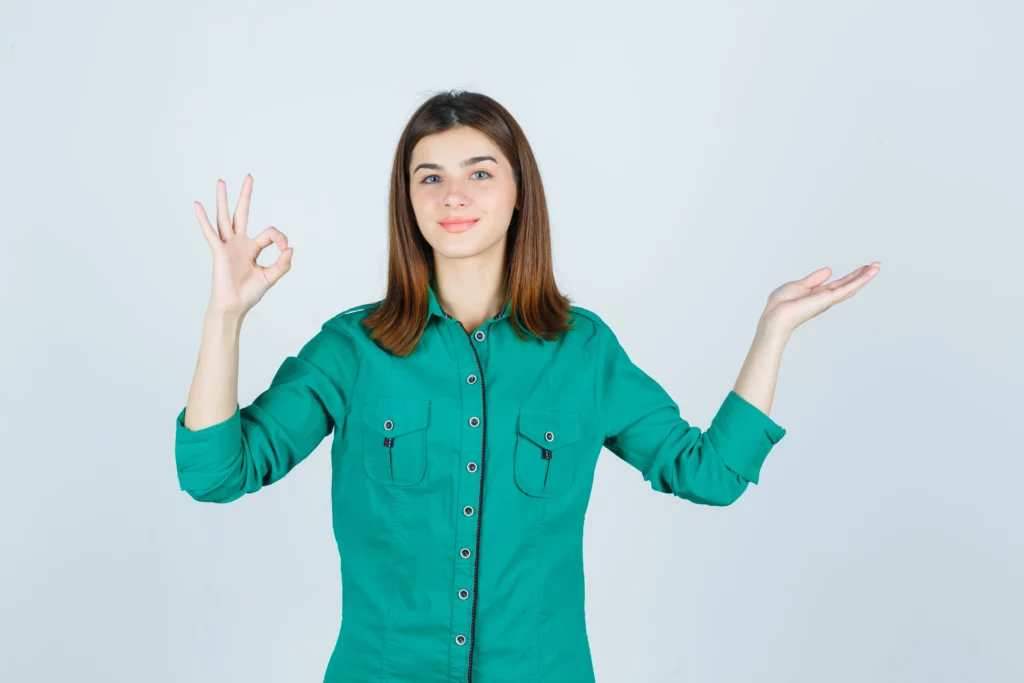 Woman in green shirt making OK sign with one hand, other hand raised.
