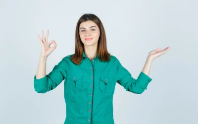 Woman in green shirt making OK sign with one hand, other hand raised.