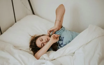 Person waking up in bed, stretching under white sheets.