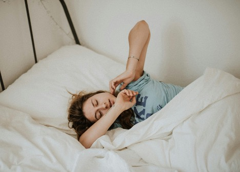 Person waking up in bed, stretching under white sheets.